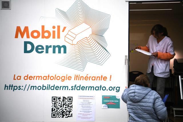 Medical assistant and truck driver Lea Fougerouge speaks with a patient ahead of an appointment with a dermatologist in an itinerant truck as part of the Mobil Derm project supported by the Societe Francaise de Dermatologie (French Dermatology Society) at a parking lot in Lafox, south-western France, on April 2, 2026. As in the rest of France, patients suffering from skin diseases are facing significant delays in receiving care in Nouvelle-Aquitaine, with loss of chances in the most serious cases. In Lafox, 25 patients a day enter the few square meters of the mobile clinic, where a dermatologist from the Basque Country has come for two days to carry out consultations in her free time  a pioneering system in France intended to compensate for the shortage of dermatologists and address medical deserts. (Photo by Christophe ARCHAMBAULT / AFP)