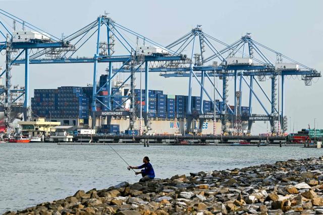 An angler fishes as a cargo ship is docked at Malaysia's North Klang port in Port Klang, on the outskirts of Kuala Lumpur on April 6, 2026. (Photo by Mohd RASFAN / AFP)