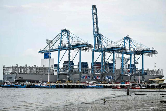 A person walks along the shore as a cargo ship is docked at Malaysia's North Klang Port in Port Klang, on the outskirts of Kuala Lumpur on April 6, 2026. (Photo by Mohd RASFAN / AFP)