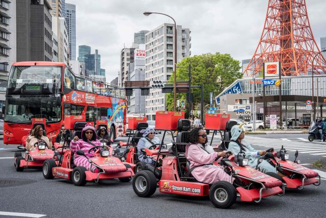 TOPSHOT - Foreign tourists drive go-karts drive past a gas station in Tokyo on April 6, 2026. (Photo by Yuichi YAMAZAKI / AFP)