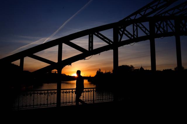 A man walks on the Debilly footbridge over the Seine river at sunrise in Paris, on April 6, 2026. (Photo by Kenzo TRIBOUILLARD / AFP)