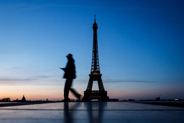 A pedestrian walks along the Esplanade du Trocadero with a view of the Eiffel Tower in the background at sunrise on April 6, 2026 in Paris. (Photo by Kenzo TRIBOUILLARD / AFP)
