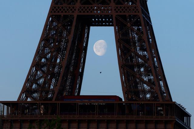 TOPSHOT - This picture shows the moon behind the Eiffel Tower in Paris on April 6, 2026. (Photo by Kenzo TRIBOUILLARD / AFP)