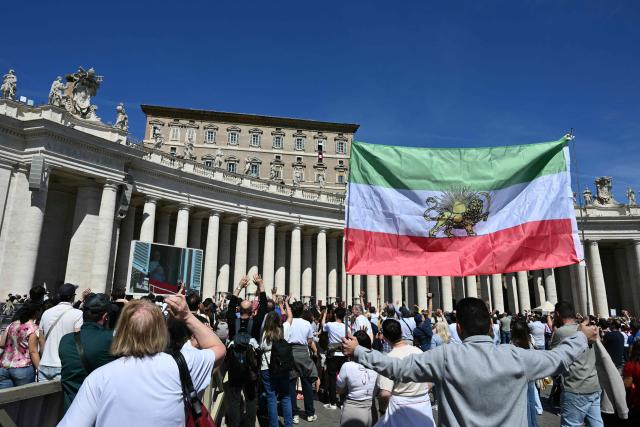 A man holds the Iranian prerevolution lion and sun flag as Pope Leo XIV addresses the crowd from the window of the apostolic palace overlooking St. Peter's square during the Regina Coeli prayer in The Vatican on April 6, 2026. (Photo by Alberto PIZZOLI / AFP)