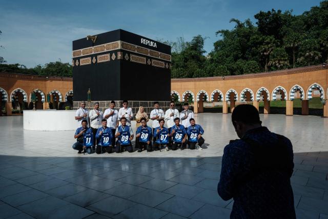 Travel agents pose in front of a replica of the Kaaba, Islam’s holiest shrine, as they bring as prospective Indonesian pilgrims at the Al Mahmudah Manasik Training Center (AMTC) in South Tangerang on April 5, 2026. The centre provides a simulated experience of Mecca’s pilgrimage sites ahead of the Hajj season in late May. Indonesia, home to the world’s largest Muslim population, has been allocated a Hajj quota of 221,000 pilgrims for 2026, but faces long waiting lists that can stretch for decades in some regions. (Photo by YASUYOSHI CHIBA / AFP)