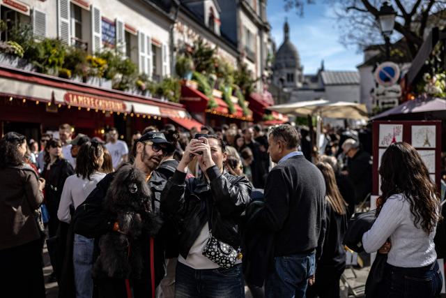 Two pedestrians holding a dog take a selfie amid the crowded Place du Tertre near the Sacre Coeur Basilica atop Montmartre hill, on Easter Monday in Paris on April 6, 2026. (Photo by Ian LANGSDON / AFP)
