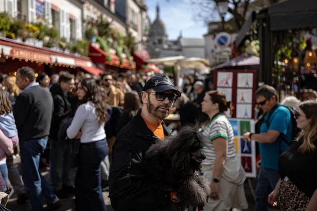 A pedestrian holding a dog walks across the crowded Place du Tertre the Sacre Coeur Basilica atop Montmartre hill, on Easter Monday in Paris on April 6, 2026. (Photo by Ian LANGSDON / AFP)
