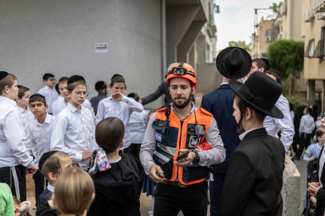 A first responder walks between children gathered to look at a building that was hit by an Iranian projectile attack in Bnei Brak in central Israel on April 6, 2026. Israeli strikes killed the intelligence chief of Iran's Revolutionary Guards, as the Islamic republic on April 6 defied threats from the US President to devastate civilian infrastructure if it does not reopen the Strait of Hormuz. (Photo by Ilia YEFIMOVICH / AFP) / 