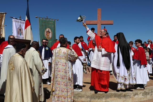 Bishop of Ajaccio, Cardinal Francois Bustillo (C), blesses worshippers in front of a cross as brotherhoods members prepare to shoost rifles as part of a procession on Easter Monday in Cargese, the French Mediterranean island of Corsica, on April 6, 2026. (Photo by Pascal POCHARD-CASABIANCA / AFP)