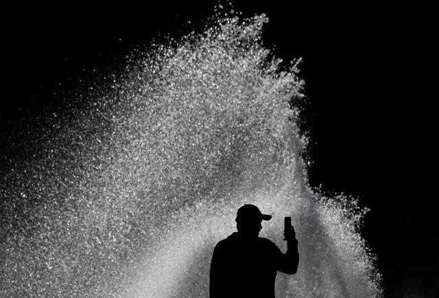 A man shoots a video on his mobile phone as a gust of wind scatters the water of a fountain in Berlin on April 6, 2026. (Photo by John MACDOUGALL / AFP)