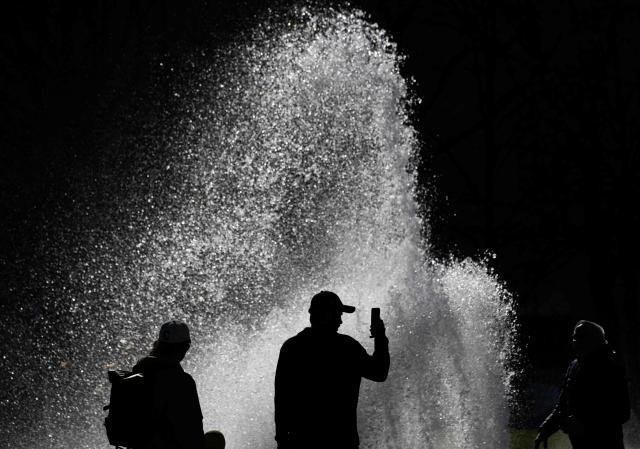 A man shoots a video on his mobile phone as a gust of wind scatters the water of a fountain in Berlin on April 6, 2026. (Photo by John MACDOUGALL / AFP)