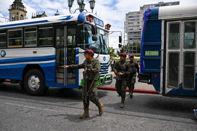 Guatemalan soldiers walk between parked buses as part of a protest by transport operators in front of the Culture Palace in Guatemala City on April 6, 2026. Transport operators call for the Guatemalan government's help in the face of rising fuel and oil derivative prices due to the Middle East crisis. (Photo by Johan ORDÓÑEZ / AFP)