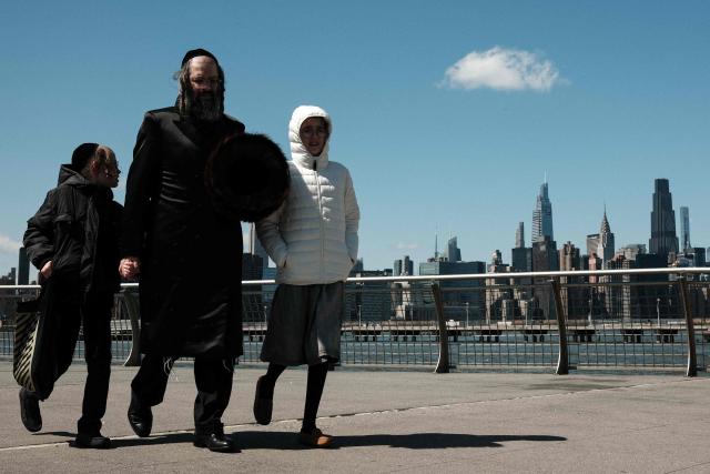An Ultra-Orthodox Jewish father and his children walk in the Brooklyn borough of New York City backdropped by the Manhattan skyline on April 6, 2026. (Photo by CHARLY TRIBALLEAU / AFP)