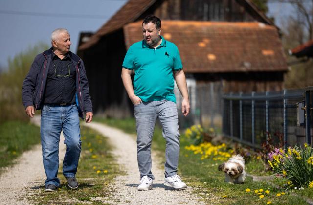 Juraj Pievac (70), accompanied by his son Ivan (43) and dog Zeus, walks towards his house not far from the place where he was injured by a mine explosion, in the village of Brodani near Karlovac on March 24, 2026. More than 30 years after the independence war, that left behind around 107,000 landmines and 470,000 unexploded ordnances, Croatia is declared mine-free, a historic milestone for the country. (Photo by MARKO PERKOV / AFP)