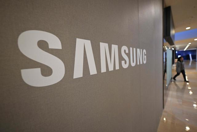 A woman walks past the logo of Samsung Electronics displayed at the company's Seocho building in Seoul on April 7, 2026. Tech giant Samsung Electronics estimated on April 7 that its first quarter profit had soared 755 percent annually to a record high of 57.2 trillion won (37.9 billion USD), driven by strong sales of chips crucial for artificial intelligence. (Photo by Jung Yeon-je / AFP)