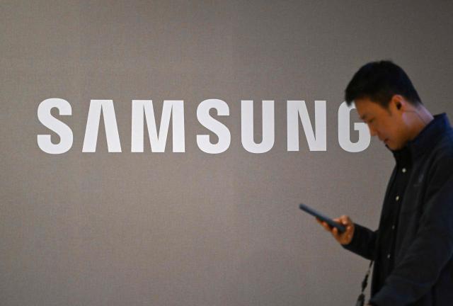 A man walks past the logo of Samsung Electronics displayed at the company's Seocho building in Seoul on April 7, 2026. Tech giant Samsung Electronics estimated on April 7 that its first quarter profit had soared 755 percent annually to a record high of 57.2 trillion won (37.9 billion USD), driven by strong sales of chips crucial for artificial intelligence. (Photo by Jung Yeon-je / AFP)