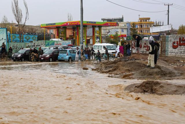 Afghan commuters ride past a gas station as they wade through a flooded street in Ghazni on April 6, 2026. Heavy rain and storms have killed at least 121 people over two weeks across Afghanistan and Pakistan, disaster officials in both countries said April 4. (Photo by Mohammad Faisal NAWEED / AFP)