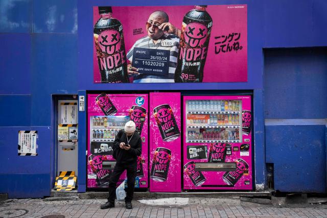 A man checks his phone in front of vending machines in Tokyo on April 7, 2026. (Photo by Yuichi YAMAZAKI / AFP)
