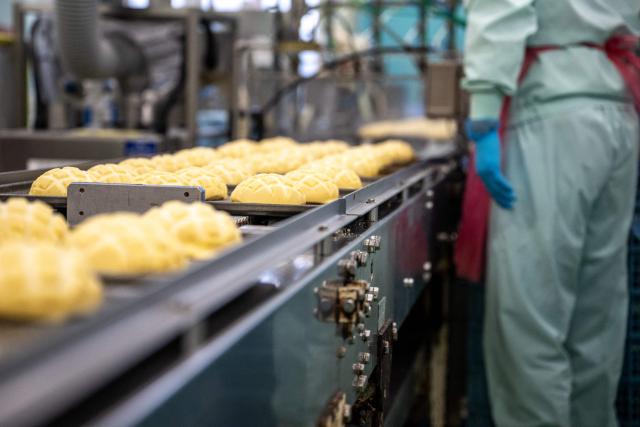 A staff member seasons the Melonpan during a media tour at the factory of Garden Bakery in Akishima city, the western portion of the Tokyo Metropolis on April 7, 2026. (Photo by Philip FONG / AFP)