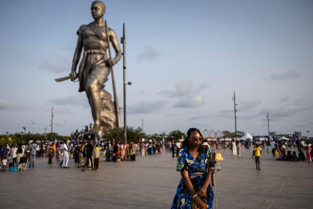 A visitor poses for a photograph next o the Amazon Statue in Cotonou on April 6, 2026. (Photo by OLYMPIA DE MAISMONT / AFP)