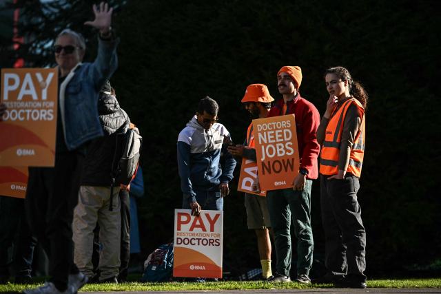 Staff members hold placards during the first day of a six-day resident doctors' strike outside the Manchester University NHS Foundation Trust in Manchester, north-west England on April 7, 2026. Doctors in England walked out for the 15th time in just over three years on April 7 in an increasingly bitter dispute with the government over pay and jobs. (Photo by Paul ELLIS / AFP)
