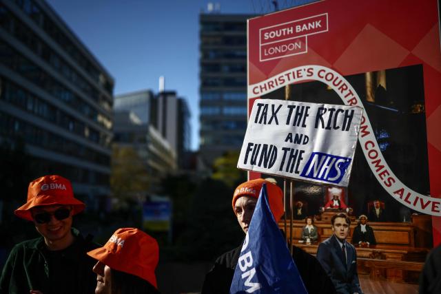 Staff members hold placards as they stand on a picket line during the first day of a six-day resident doctors' strike outside St Thomas' Hospital in central London on April 7, 2026. Doctors in England walked out for the 15th time in just over three years on April 7 in an increasingly bitter dispute with the government over pay and jobs. (Photo by Henry NICHOLLS / AFP)