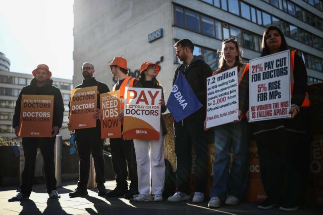 Staff members hold placards as they stand on a picket line during the first day of a six-day resident doctors' strike outside St Thomas' Hospital in central London on April 7, 2026. Doctors in England walked out for the 15th time in just over three years on April 7 in an increasingly bitter dispute with the government over pay and jobs. (Photo by Henry NICHOLLS / AFP)