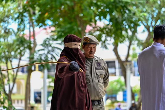 A member of Aceh's Sharia police lashes a man (R) during a public flogging in Banda Aceh on April 7, 2026. A couple was publicly flogged in Indonesia's staunchly Islamic Aceh province on April 7 for having sex outside of marriage, an AFP reporter witnessed, in the country's only region to apply a version of Sharia law. Sexual relations between unmarried people are outlawed in Aceh. (Photo by CHAIDEER MAHYUDDIN / AFP)