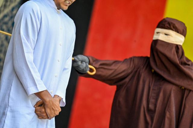 A man (L) reacts during a public flogging held by Aceh's Sharia police in Banda Aceh on April 7, 2026. A couple was publicly flogged in Indonesia's staunchly Islamic Aceh province on April 7 for having sex outside of marriage, an AFP reporter witnessed, in the country's only region to apply a version of Sharia law. Sexual relations between unmarried people are outlawed in Aceh. (Photo by CHAIDEER MAHYUDDIN / AFP)