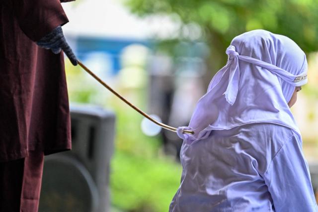 A woman (R) reacts during a public flogging held by Aceh's Sharia police in Banda Aceh on April 7, 2026. A couple was publicly flogged in Indonesia's staunchly Islamic Aceh province on April 7 for having sex outside of marriage, an AFP reporter witnessed, in the country's only region to apply a version of Sharia law. Sexual relations between unmarried people are outlawed in Aceh. (Photo by CHAIDEER MAHYUDDIN / AFP)