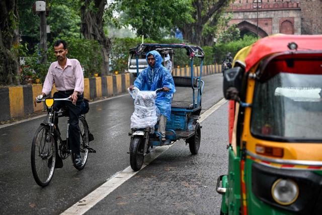 A rickshaw driver shields himself with a plastic poncho while riding through the rain in the old quarters of Delhi on April 7, 2026. (Photo by Sajjad HUSSAIN / AFP)