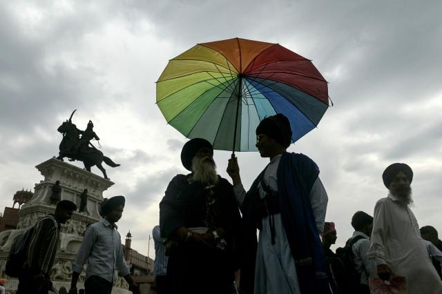 Sikh men sharing an umbrella stand near the statue of Maharaja Ranjit Singh as dark clouds loom over Amritsar on April 7, 2026. (Photo by Narinder NANU / AFP)