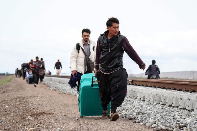 Afghan migrants carrying their belongings walk along the Khaf–Herat railway beside the flooded road in the Zendeh Jan district of Herat on April 6, 2026 after returning from Iran. In Afghanistan, which already faces a severe humanitarian crisis, rain, floods, landslides and lightning strikes killed 123 people since March 26, the spokesman of the national disaster management authority, Mohammad Yousuf Hammad, told AFP. (Photo by Mohsen KARIMI / AFP)