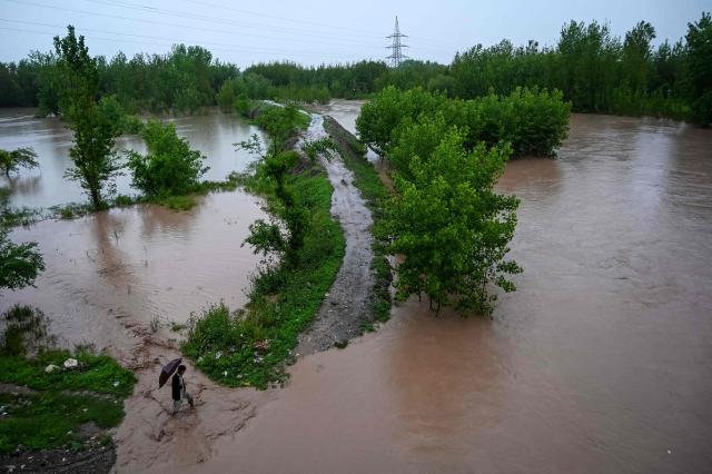 A man walks along a flooded path as torrential rains cause water channels to overflow, inundating nearby areas of Peshawar on April 7, 2026. Heavy rain, storms, and floods have battered Afghanistan and neighbouring Pakistan for more than two weeks, killing at least 188 people, disaster officials in both countries said on April 7, 2026. (Photo by Abdul MAJEED / AFP)