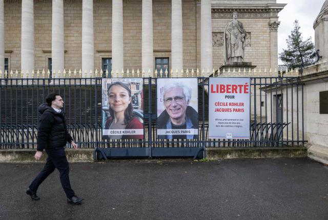 (FILES) A pedestrian walks past portrait placards of Cecile Kohler and Jacques Paris, two French citizens formerly detained in Iran, set up on a fence of the French National Assembly, in Paris on March 11, 2026. Emmanuel Macron announced on April 7, 2026 that the French nationals Cecile Kohler and Jacques Paris ‘are free and on their way to French territory, after three and a half years in detention in Iran’, where they had spent a long time in prison before being placed under house arrest at the French embassy. (Photo by Martin LELIEVRE / AFP)