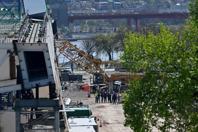 Construction workers stand by the scene where a crane collapsed at the construction site of a new bridge, on the banks of the River Sava in Belgrade on April 7, 2026. The collapsing of the 350-ton metal structure left one person dead while three others were injured, according to the Serbian Interior Ministry and Serbian media. The circumstances surrounding the incident are currently under investigation by the authorities. (Photo by Andrej ISAKOVIC / AFP)