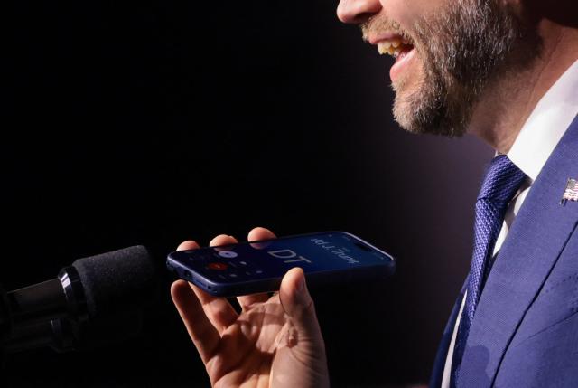 US Vice President JD Vance holds a mobile phone while on a call with US President Donald Trump to a microphone during a "Day of Friendship" event with Hungarian Prime Minister Viktor Orban (not in picture) at MTK Sportpark in Budapest, Hungary on April 7, 2026. US Vice President JD Vance is in Hungary to deliver the US President's support to his ally, nationalist Prime Minister Viktor Orban, ahead of tightly contested parliamentary elections scheduled for April 12, 2026. (Photo by Jonathan Ernst / POOL / AFP)