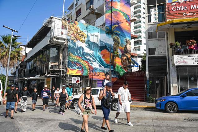 Tourists walk past a mural by Mexican artist Ivan Bailon Hernandez titled "Sueno Mundialista" (World Cup dream), referring to the upcoming FIFA World Cup 2026, in Acapulco, Guerrero state, Mexico, on April 7, 2026. (Photo by Faustine FRANCISCO / AFP)