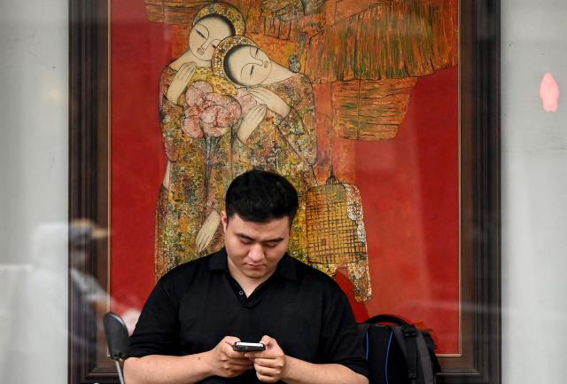 A man uses his phone in front of a lacquer painting in Hanoi on April 8, 2026. (Photo by Nhac NGUYEN / AFP)
