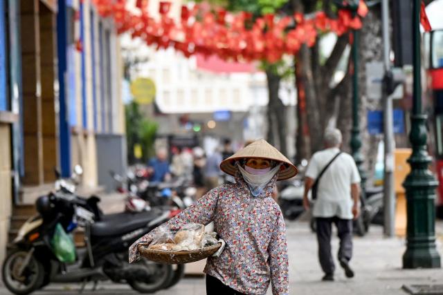 A street vendor walks down a street in Hanoi carrying food for sale on April 8, 2026. (Photo by Nhac NGUYEN / AFP)