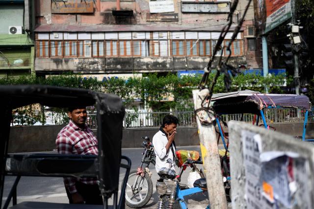 A rickshaw driver smokes a cigarette as he waits for customers along a street in the old quarters of Delhi on April 8, 2026. (Photo by MANAN VATSYAYANA / AFP)