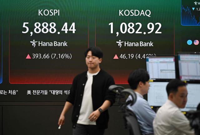 A currency dealer walks past a screen showing South Korea's benchmark stock index (KOSPI) and the Korean Securities Dealers Automated Quotations (KOSDAQ) in a foreign exchange dealing room at the Hana Bank headquarters in Seoul on April 8, 2026. (Photo by Jung Yeon-je / AFP)