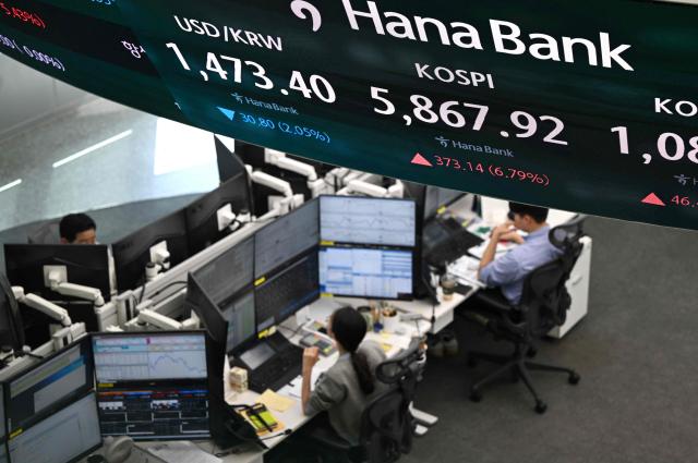 Currency dealers monitor exchange rates as a screen shows South Korea's benchmark stock index (KOSPI) and the Korean won/USD exchange rate in a foreign exchange dealing room at the Hana Bank headquarters in Seoul on April 8, 2026. (Photo by Jung Yeon-je / AFP)