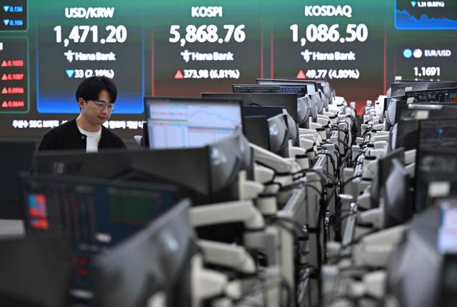 A currency dealer monitors exchange rates as a screen shows South Korea's benchmark stock index (KOSPI) in a foreign exchange dealing room at the Hana Bank headquarters in Seoul on April 8, 2026. (Photo by Jung Yeon-je / AFP)