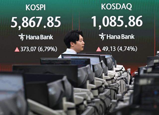 A currency dealer walks past a screen showing South Korea's benchmark stock index (KOSPI) and the Korean Securities Dealers Automated Quotations (KOSDAQ) in a foreign exchange dealing room at the Hana Bank headquarters in Seoul on April 8, 2026. (Photo by Jung Yeon-je / AFP)