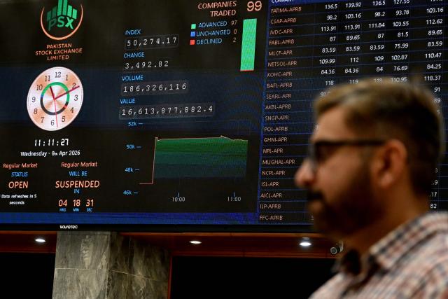 A stockbroker walks past share prices on a digital board during a trading session at the Pakistan Stock Exchange (PSX) in Karachi on April 8, 2026. (Photo by Rizwan TABASSUM / AFP)