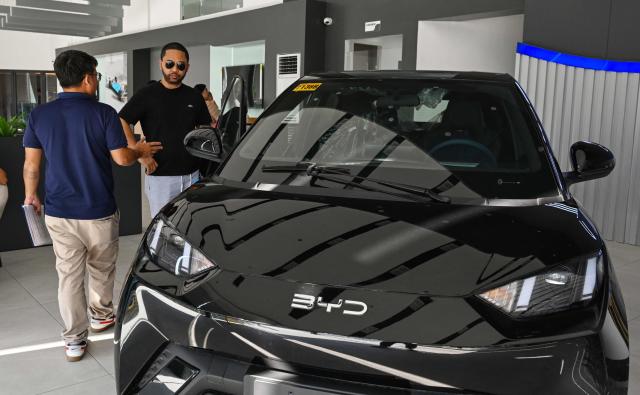 A man talks to a salesman beside a BYD electric car at a dealership in Dasmarinas, province of Cavite on April 8, 2026. (Photo by Jam STA ROSA / AFP)