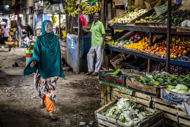 A woman walks past a vegetable stall in an open-air market as residents gather in the streets during the cooler evening hours to escape the daytime heat in downtown Djibouti, on April 7, 2026, ahead of the 2026 Djiboutian presidential elections. (Photo by Luis TATO / AFP)