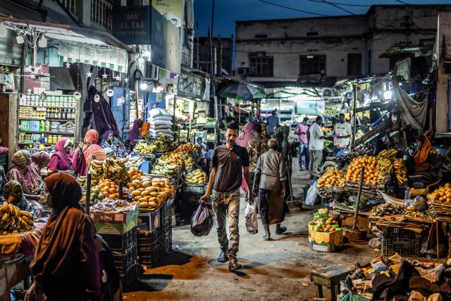 Marketgoers move through an open-air market as residents gather in the streets during the cooler evening hours to escape the daytime heat in downtown Djibouti, on April 7, 2026, ahead of the 2026 Djiboutian presidential elections. (Photo by Luis TATO / AFP)