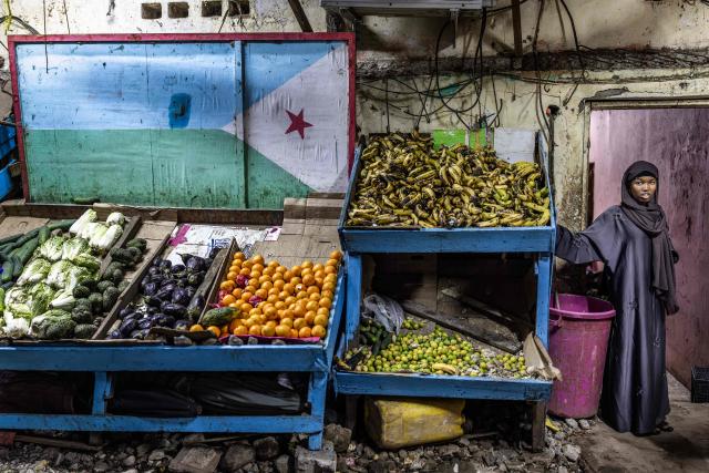 TOPSHOT - A woman stands beside a stall decorated with the Djiboutian flag in an open-air market as residents take to the streets during the cooler evening hours to escape the daytime heat in downtown Djibouti, on April 7, 2026, ahead of the 2026 Djiboutian presidential elections. (Photo by Luis TATO / AFP)